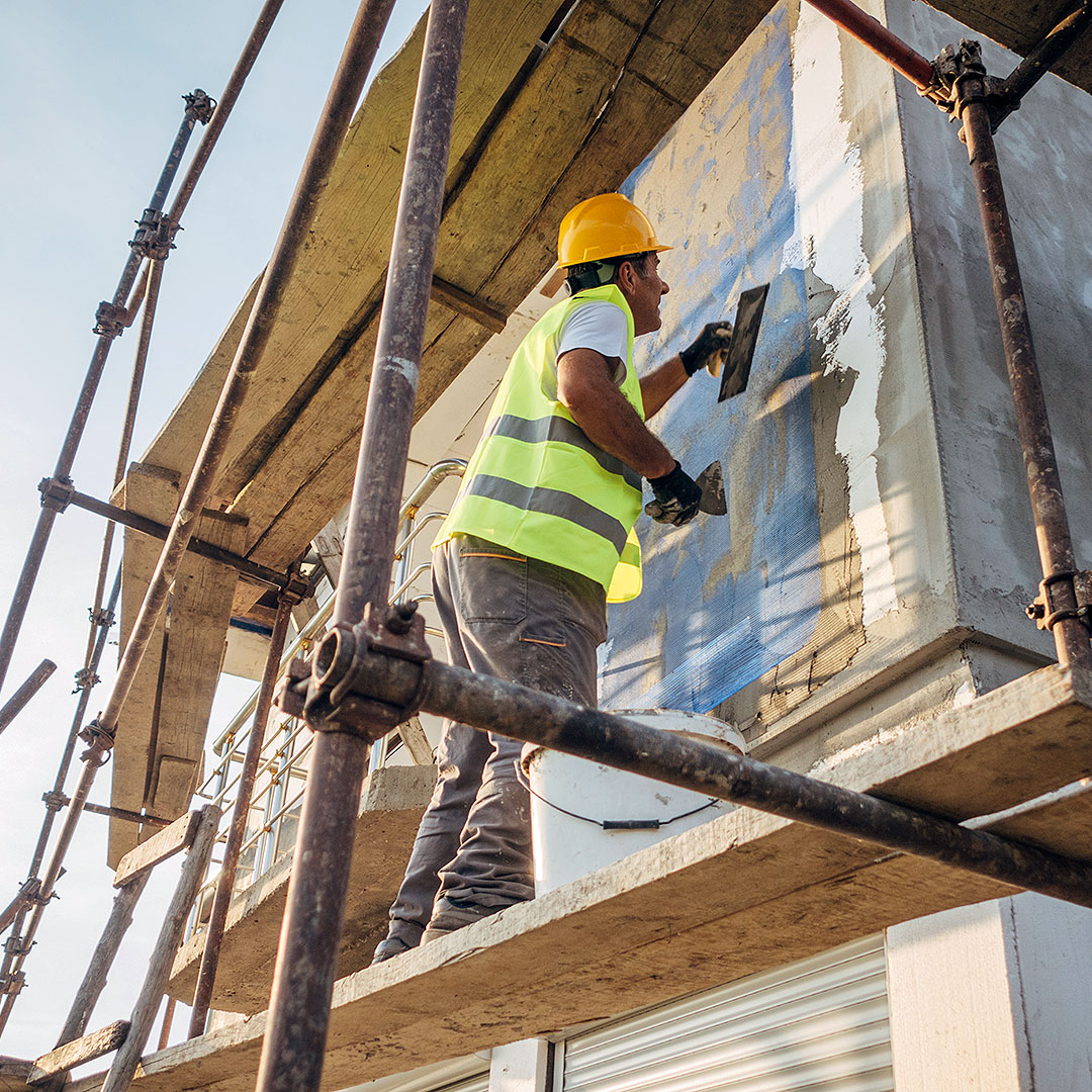 Ein Bauarbeiter steht auf einem Gerüst und bereitet eine Fassade für die energetischen Sanierung vor.